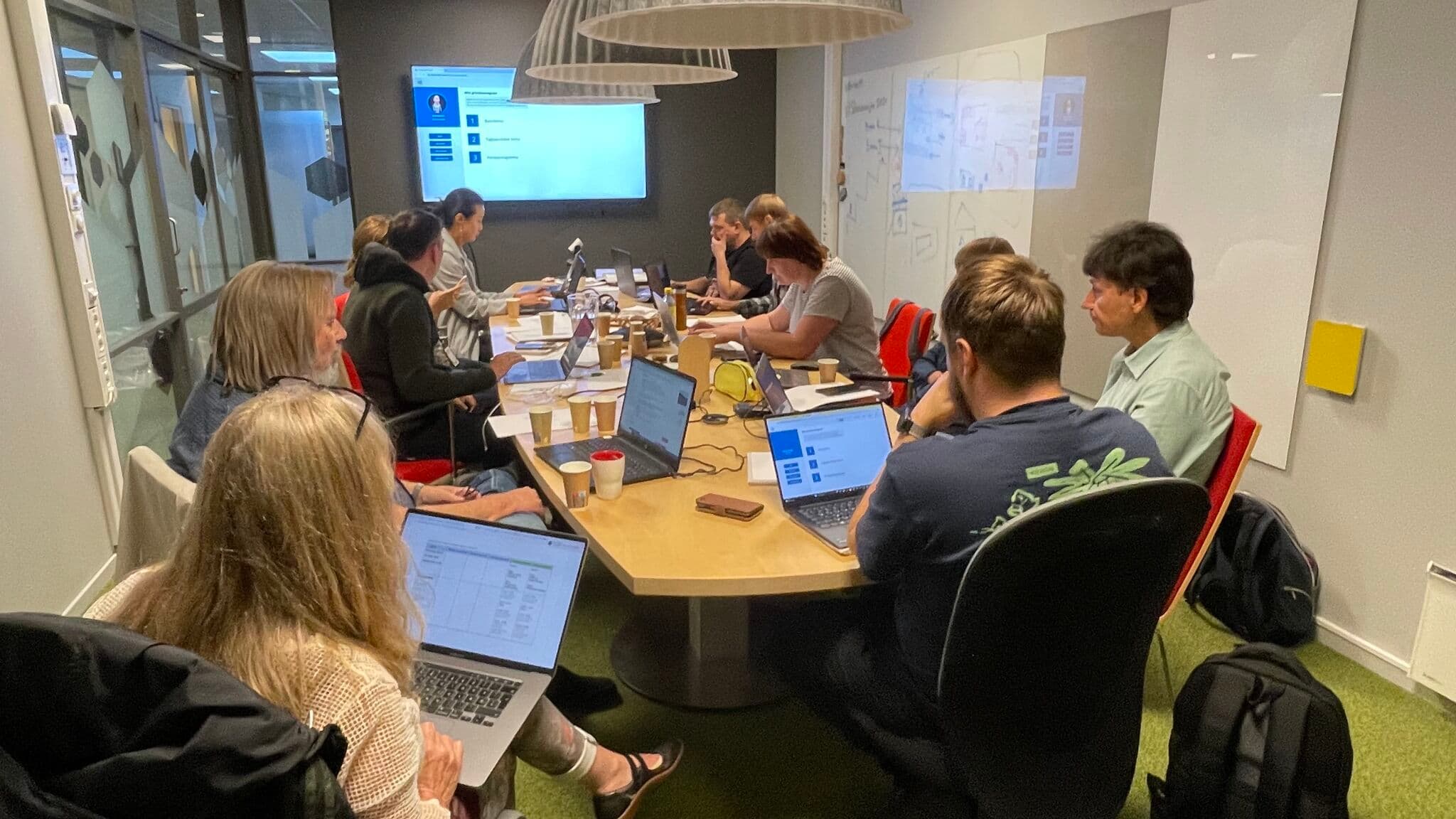 Deltakere arbeider med digitale verktøy og oppgaver rundt et felles bord.
